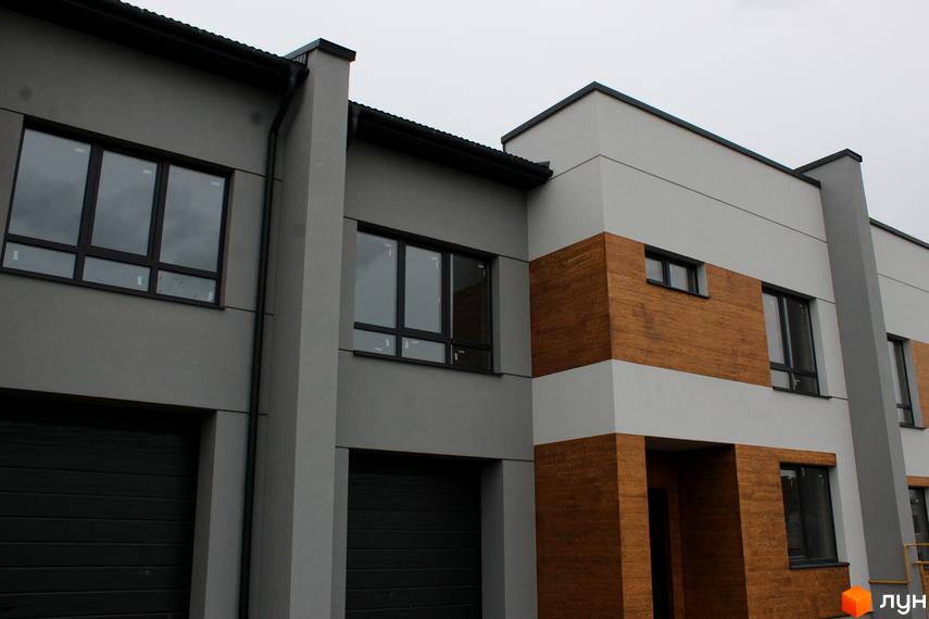 Фасад таунхаусу «Пронятин» з сірими стінами, чорними вікнами та гаражними дверима. Житловий комплекс з сучасним дизайном та зручним розташуванням.