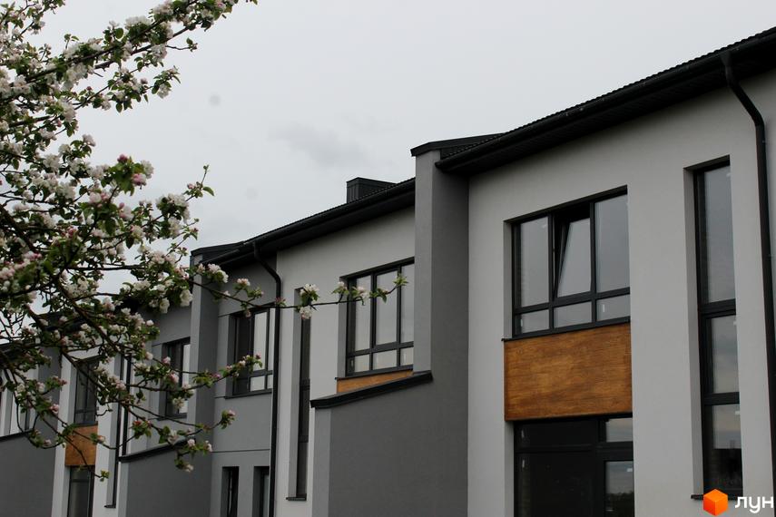 Фасад таунхаусів ЖК «Пронятин» з великими вікнами та оздобленням деревом. На передньому плані гілки квітучого дерева, що додає природності.