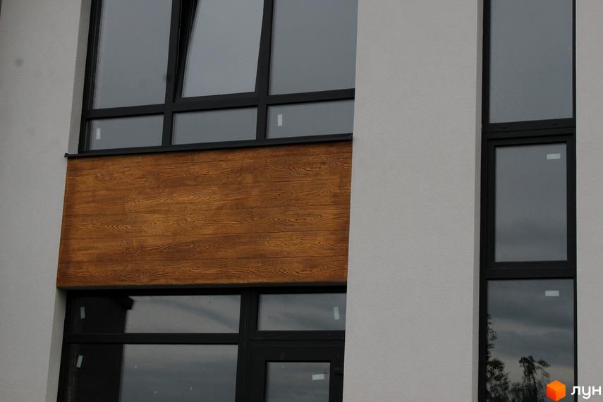 Фасад будинку ЖК „Пронятин“ з великими вікнами та оздобленням з дерева. Засклені вікна відображають небо та навколишнє середовище.