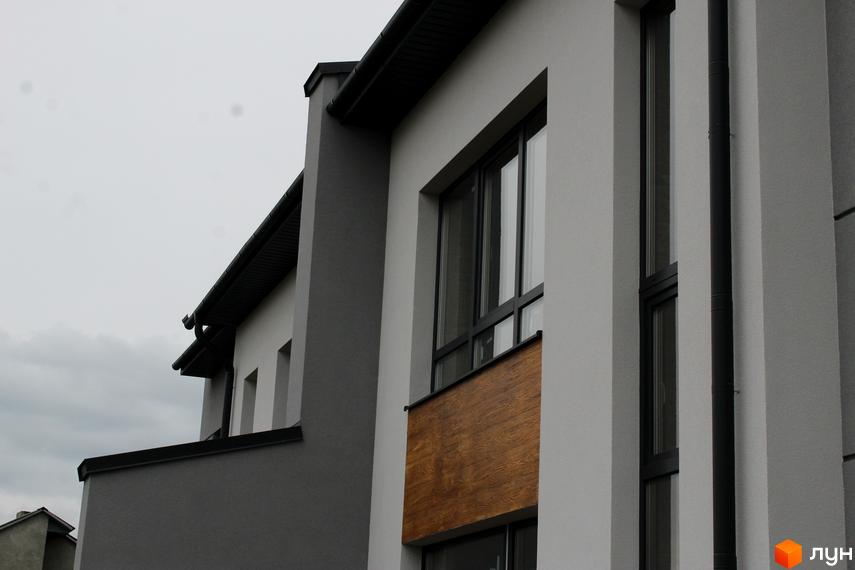 Фасад Таунхаус Пронятин з сіро-білим оздобленням, великими вікнами з темними рамами та дерев'яними панелями. Видно частину темного даху.