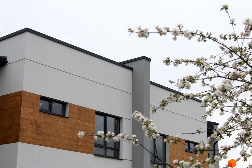 Зовнішній вигляд будинку Житловий комплекс „Пронятин“ з дерев'яною обробкою фасаду та квітучими деревами на передньому плані.