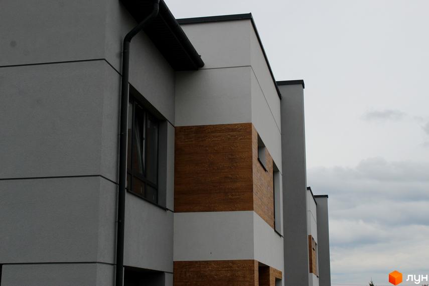Зображення фасаду Таунхаус „Пронятин“ з комбінованою обробкою: сірі та білі стіни з дерев'яними вставками, темні вікна.