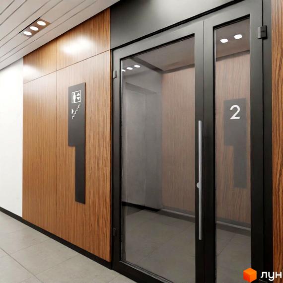 Житловий комплекс Бетховен: сучасний вхід до ліфта з дерев'яними панелями та скляними дверима. На стіні розташована навігаційна табличка з символами ліфта та сходів.