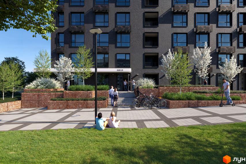 Зовнішній вигляд будинку житлового комплексу Kub29 з сірого цегли, з прибудинковою територією з зеленими насадженнями та місцями для відпочинку.