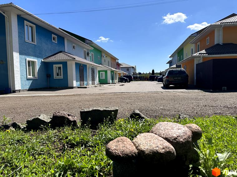 Різнокольорові таунхауси Ivankiv-townhouse з білими вікнами та дахами. Перед будинками розташований двір з парковкою та зеленими насадженнями.