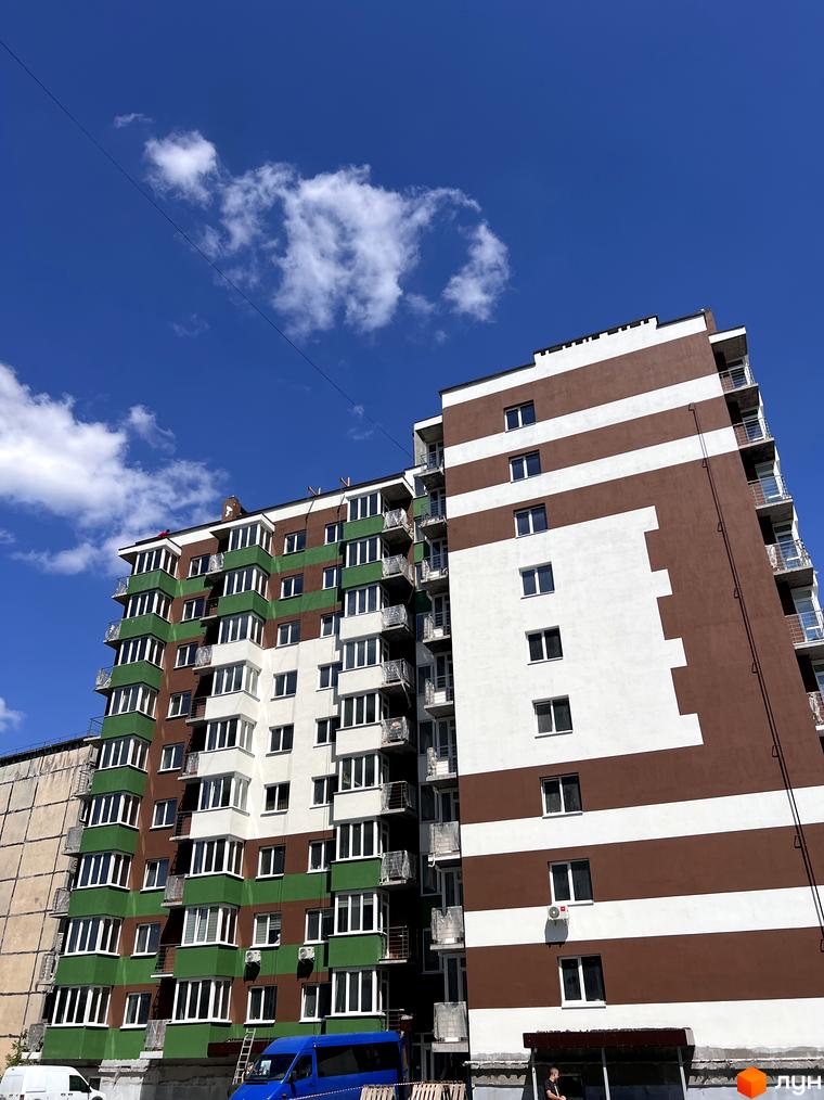 Новобудова ЖК Eco House з коричнево-білими та зелено-білими фасадами під блакитним небом з хмарами. Будинок має багато балконів та вікон.