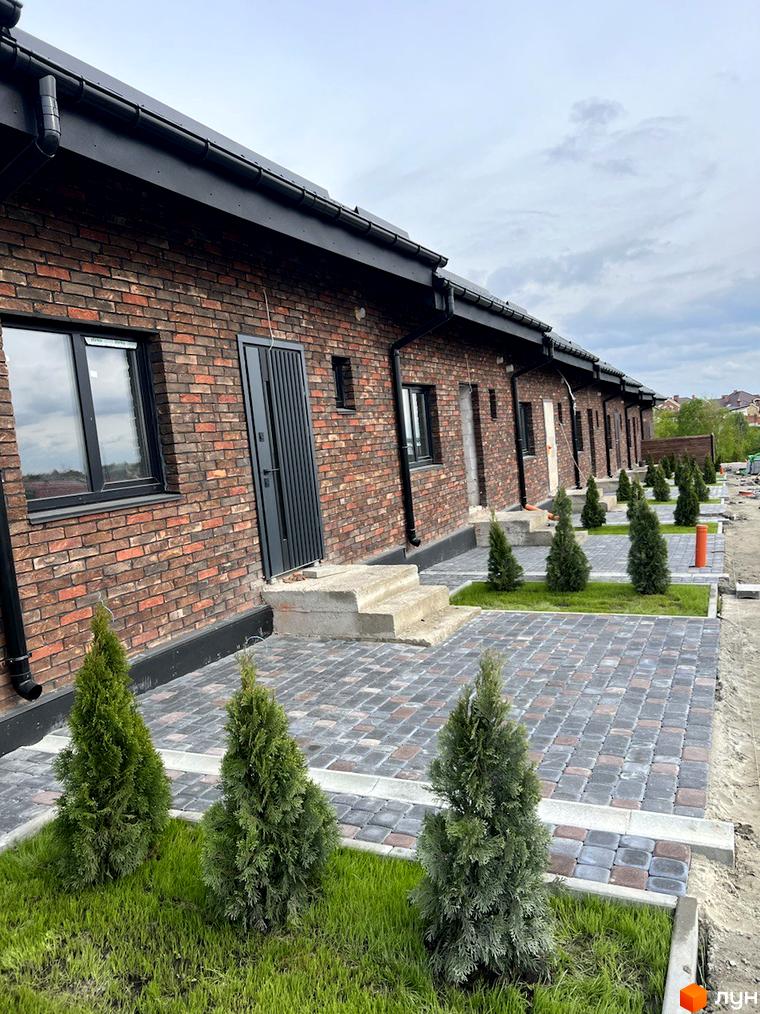 Котеджне містечко КМ Одноповерховий Київ - Гатне. Зовнішній вигляд одноповерхових будинків з цегляним фасадом та впорядкована прибудинкова територія з бруківкою та туями.