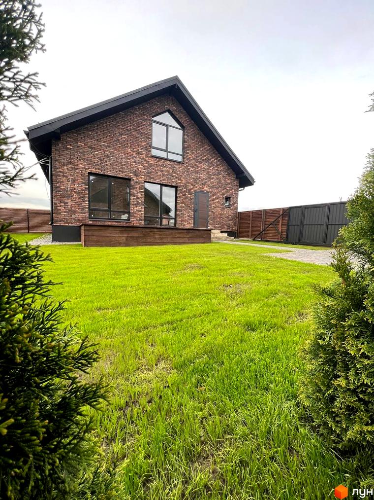 Котеджне містечко КМ Квартал Баварія: двоповерховий будинок з цегляним фасадом та великими вікнами на тлі зеленого газону та паркану.