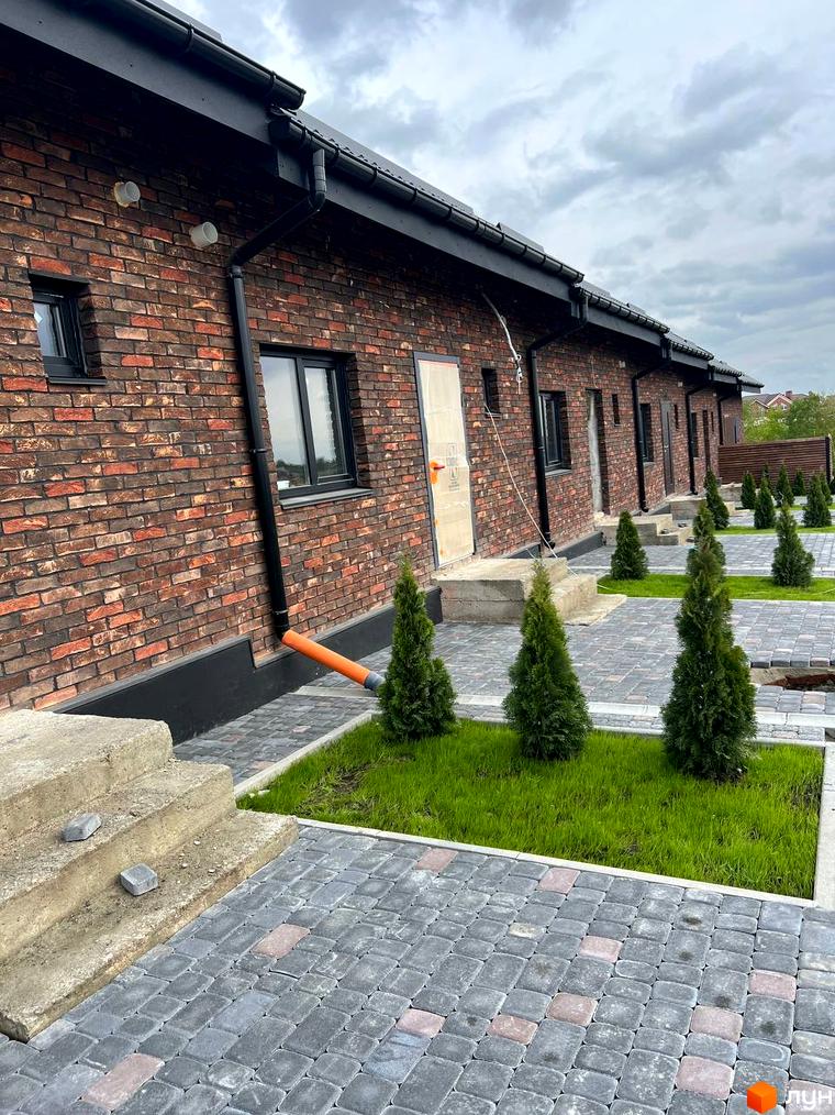 Зовнішній вигляд цегляних будинків КМ Квартал Баварія з чорними вікнами та дахом, упорядкована прибудинкова територія з бруківкою та зеленими насадженнями.