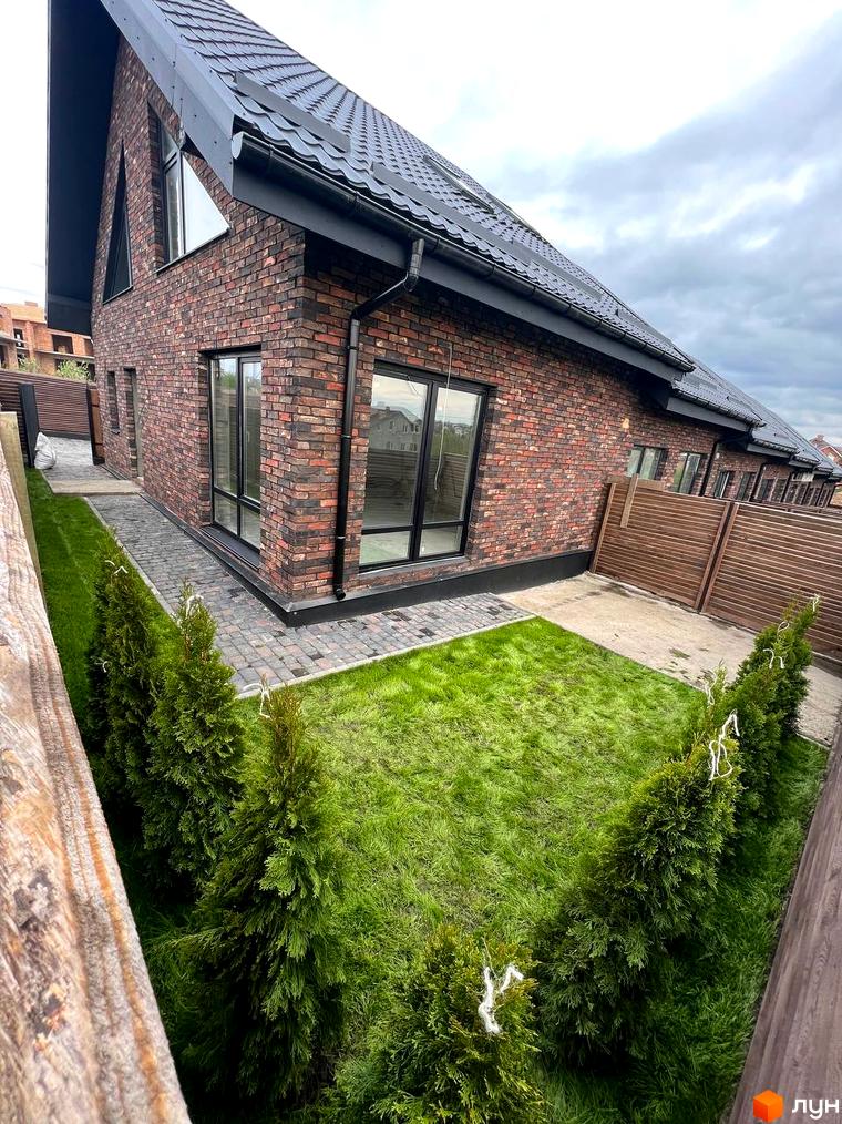 Котеджне містечко Квартал Баварія: цегляний будинок з темним дахом та акуратним газоном з туями. Прибудинкова територія з бруківкою та дерев'яним парканом.