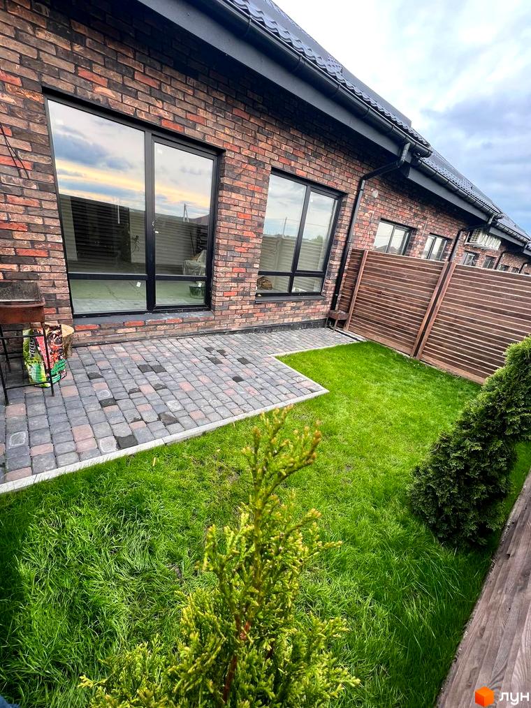 Зовнішній вигляд будинку з цегляним фасадом та великими вікнами. Прибудинкова територія з бруківкою та зеленим газоном.