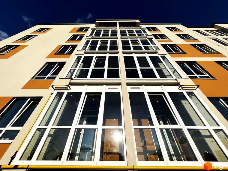 Вигляд фасаду житлового комплексу Сімейний з великою кількістю скляних балконів та панорамними вікнами. Будинок має світло-бежевий фасад з помаранчевими вставками.