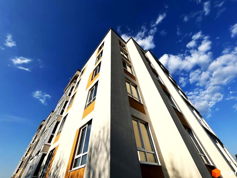 Зовнішній вигляд новобудови ЖК Сімейний з вікнами та коричневими елементами на фоні блакитного неба з хмарами. Фотографія фасаду житлового комплексу.