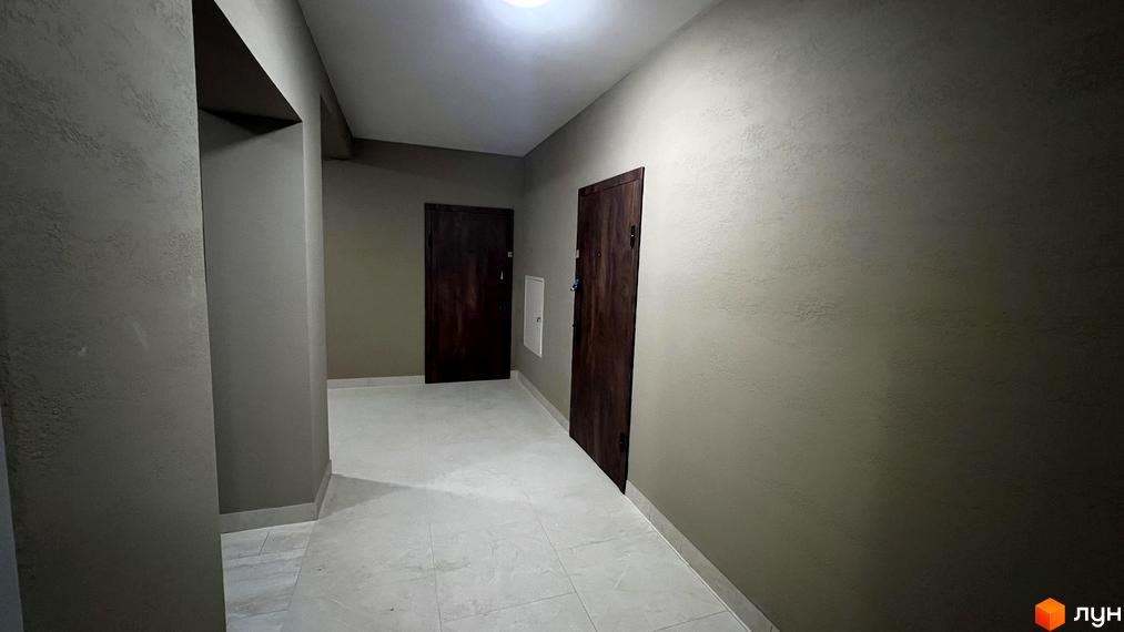 Коридор з двома дверима в житловому комплексі Сімейний. Світлі стіни та підлога, темні дерев'яні двері.