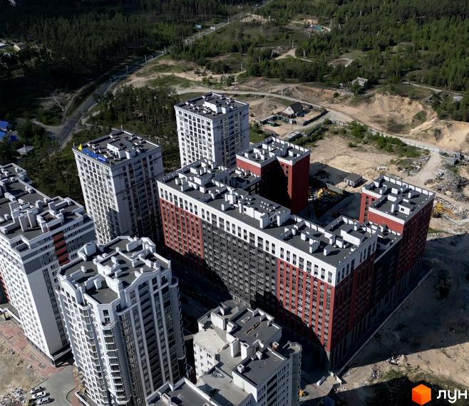 Вид на житловий комплекс Irpin City з висоти пташиного польоту. Багатоповерхові будинки з червоно-сірими фасадами та білими елементами. Навколо зелена зона та будівельні роботи.