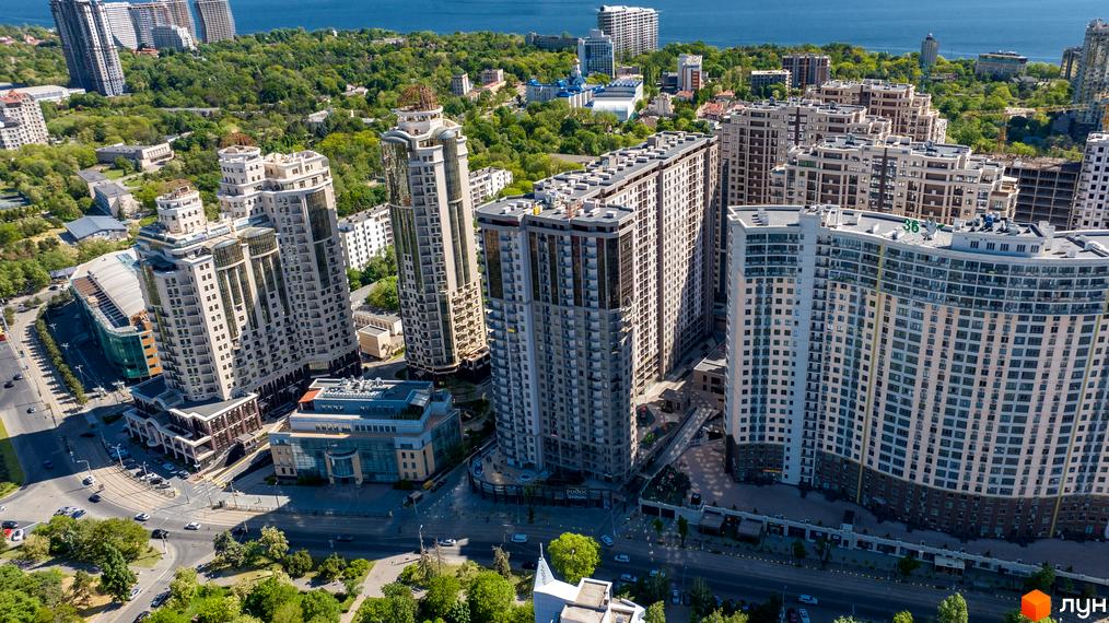 Житловий комплекс Родос: панорамний вид на висотні будівлі з балконами та світлими фасадами, оточені зеленню та дорогами, з морем на горизонті.