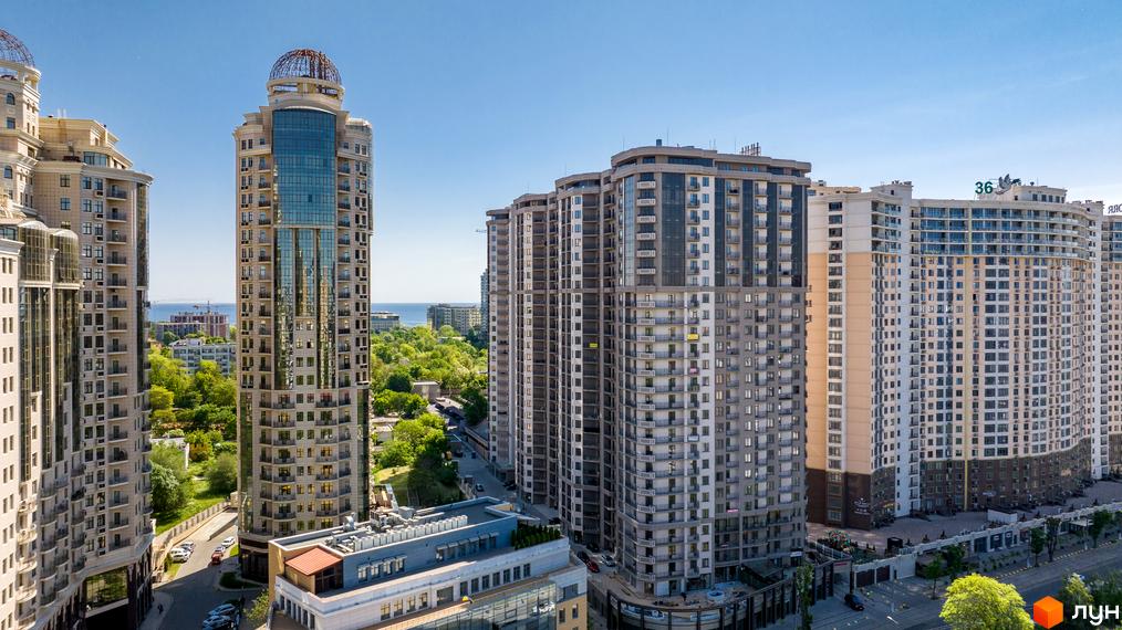 Житловий комплекс Родос: висотні житлові будинки з балконами, світлими та сірими фасадами, та один з куполом. Вид на зелень, дорогу та море.