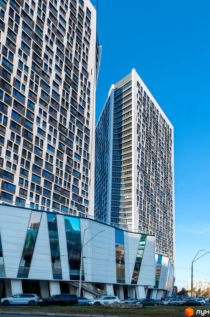 Зовнішній вигляд житлового комплексу Manhattan city: дві високі будівлі з сірими фасадами та численними вікнами. Нижня частина має кутове скління.