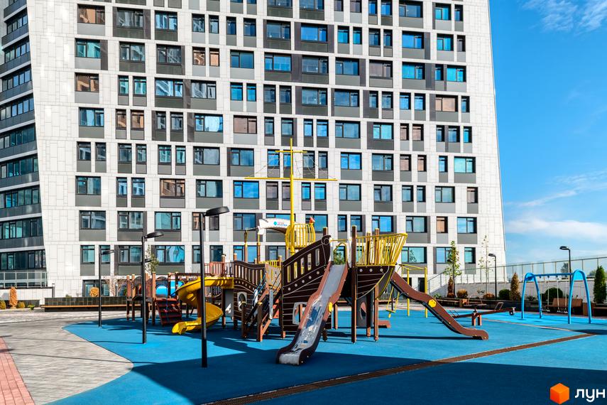 Новобудова ЖК Manhattan City з багатою прибудинковою територією та дитячим майданчиком у вигляді корабля. Сучасний житловий комплекс з великою кількістю вікон та балконів.