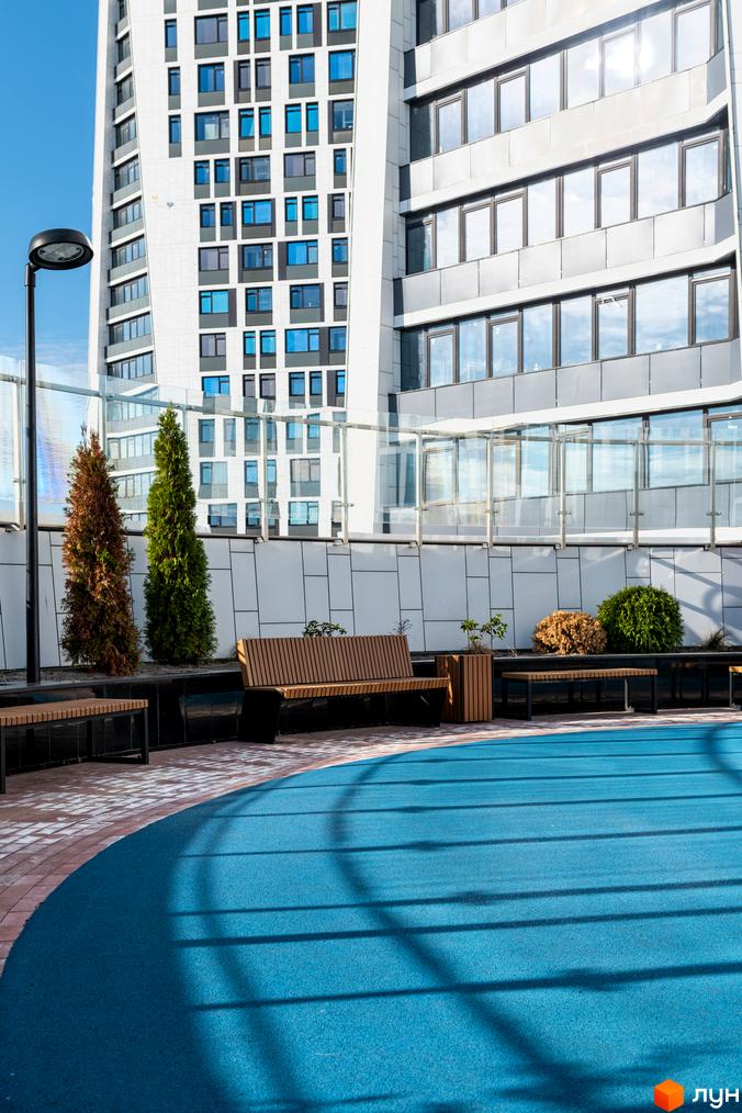 Новобудова Manhattan City з панорамними вікнами та скляним огородженням. На прибудинковій території розташовані лавки, дерева та зелені насадження.