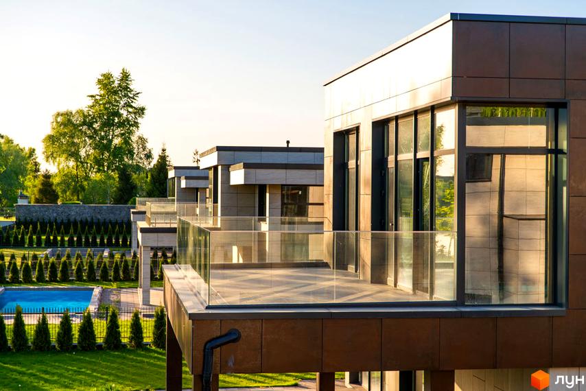 Котеджне містечко DAMBA RIVER PARK з басейном та акуратно підстриженими деревами. Сучасна архітектура будинків з великими вікнами та скляними балконами.