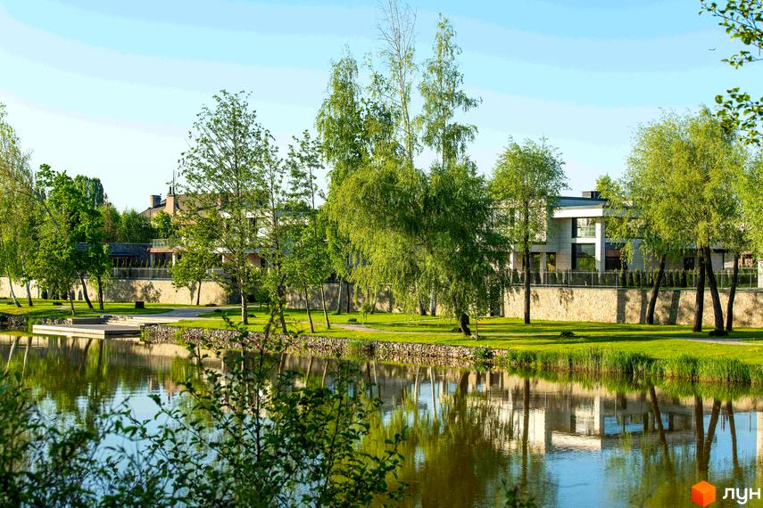 Котеджне містечко DAMBA RIVER PARK з озером та зеленими деревами. Сучасні будинки на березі водойми.