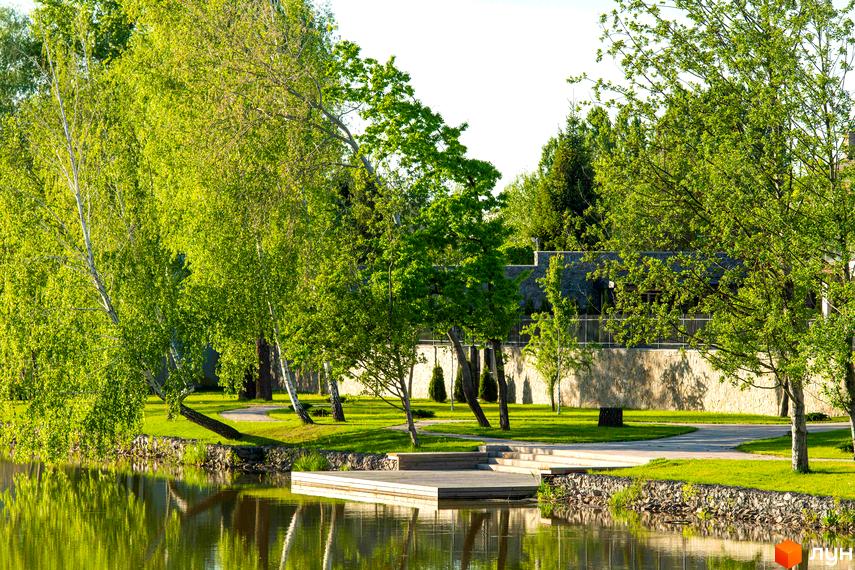 Котеджне містечко DAMBA RIVER PARK з дерев'яним пірсом на березі водойми та зеленою зоною відпочинку.