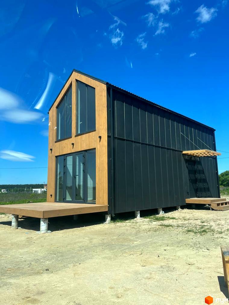 Котеджне містечко Залісся Village: двоповерховий будинок з дерев'яним та чорним фасадом, великими вікнами та терасою на опорах.