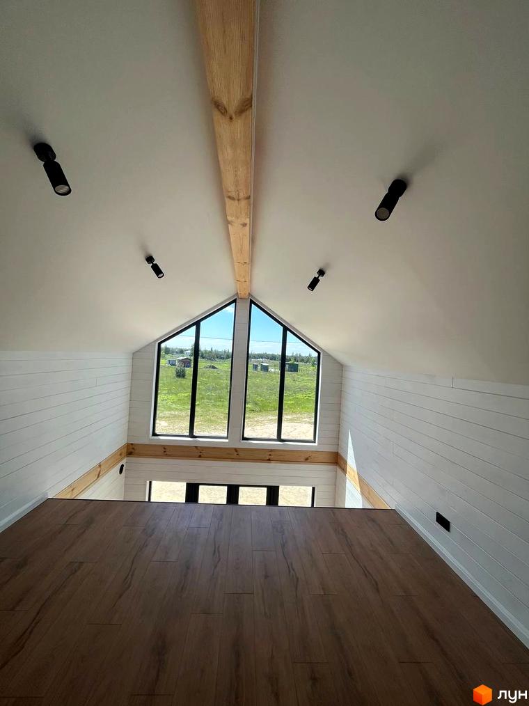 Інтер'єр мансардного поверху котеджного містечка Залісся Village з великими вікнами та дерев'яними балками. Вид на зелене поле.
