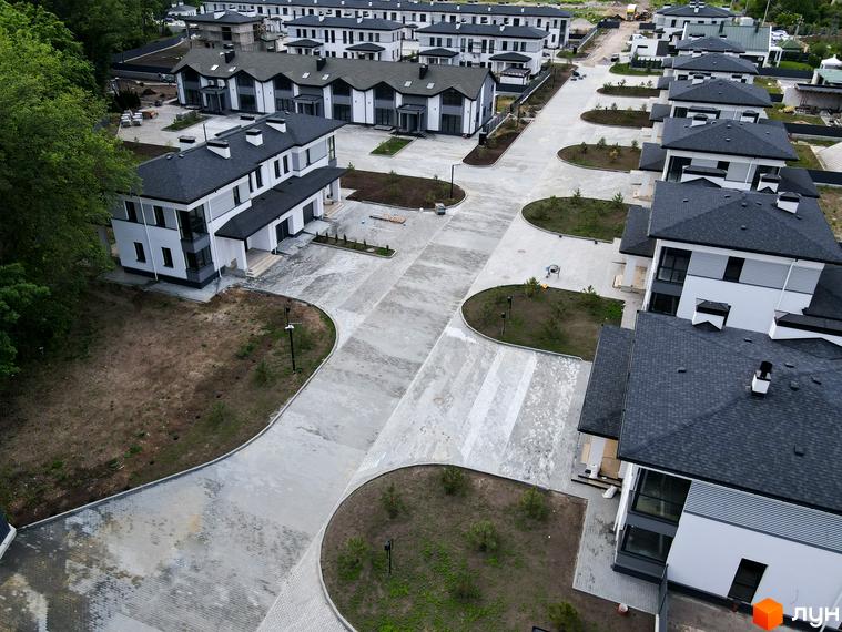 Котеджне містечко Ecopark: білі будинки з темними дахами та великими вікнами, доглянута прибудинкова територія з бруківкою та зеленими насадженнями.