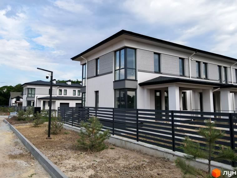 Фасад будинку в Містечку котеджів Ecopark з великими вікнами та парканом. Поруч молоді дерева та доріжка.