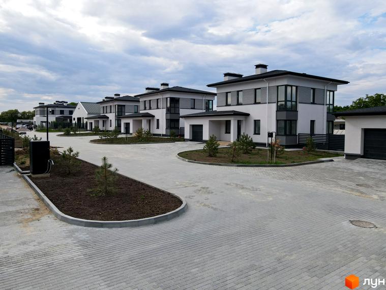 Котеджне містечко Ecopark: білі двоповерхові будинки з темними дахами та вікнами, огороджена територія з бруківкою та зеленими насадженнями.