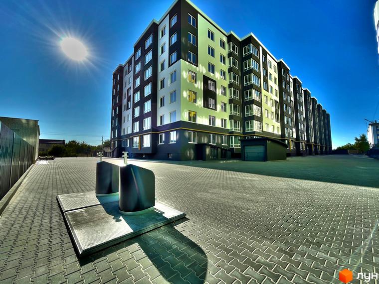 Багатоповерховий будинок житлового комплексу Петрівські Липки з великими вікнами. Територія перед будинком викладена бруківкою, сонячна погода.