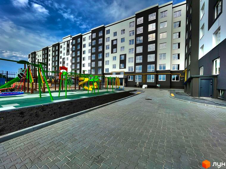 Житловий комплекс Петрівські Липки: фасад будинку з чорно-білими елементами та дитячий майданчик з гірками та гойдалками.