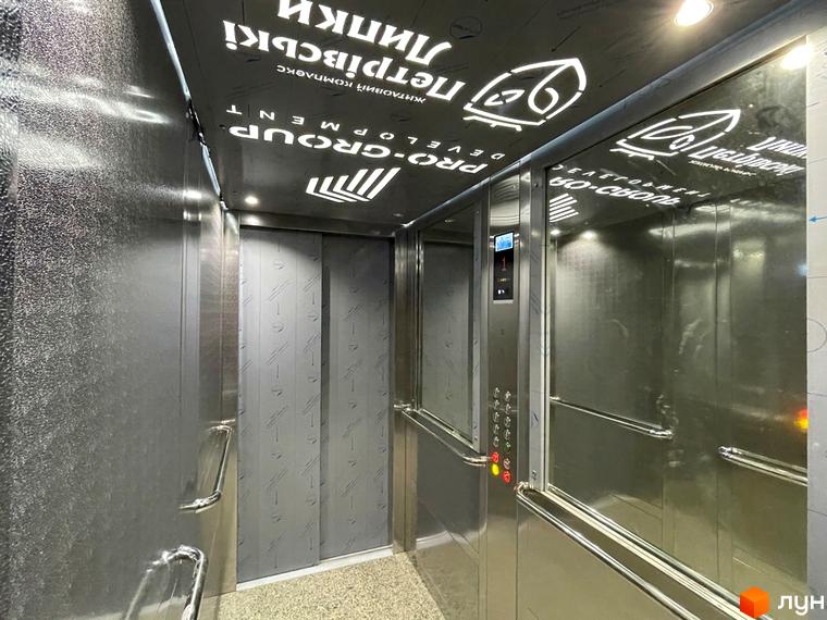 Ліфт в середині будинку Житловий комплекс Петрівські Липки. Стіни та двері ліфта виконані з металу, на стелі логотип забудовника.