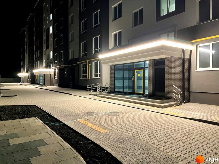 Зовнішній вигляд будинку ЖК Петрівські Липки з підсвіченим входом та бруківкою на прибудинковій території.