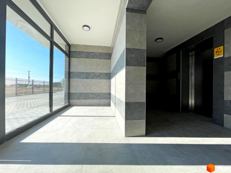 Просторий хол в ЖК Петрівські Липки з панорамними вікнами та ліфтом. Світлий інтер'єр з плиткою на стінах та підлозі.