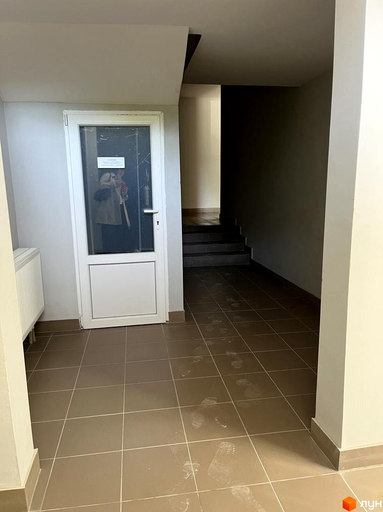 Внутрішній простір житлового комплексу на вул. Тараскова, 5: світлий коридор з білими дверима, плитковою підлогою зі слідами та сходами.