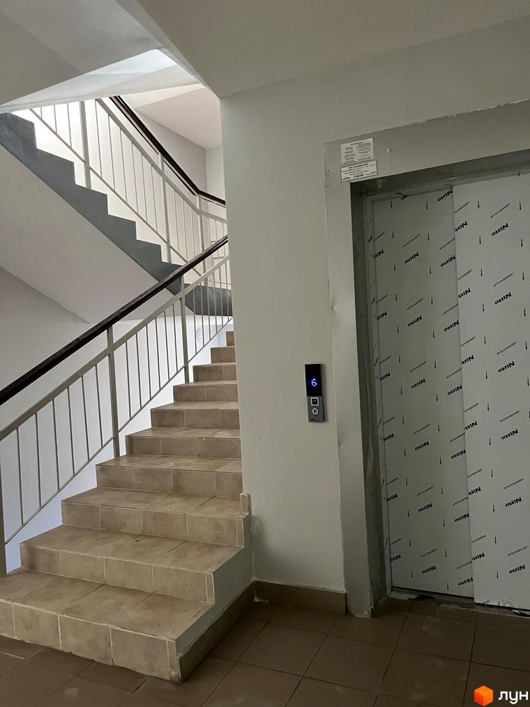 Сходи в під'їзді житлового будинку. На стіні ліфт, обклеєний захисною плівкою. На стіні панель з кнопками виклику ліфта.