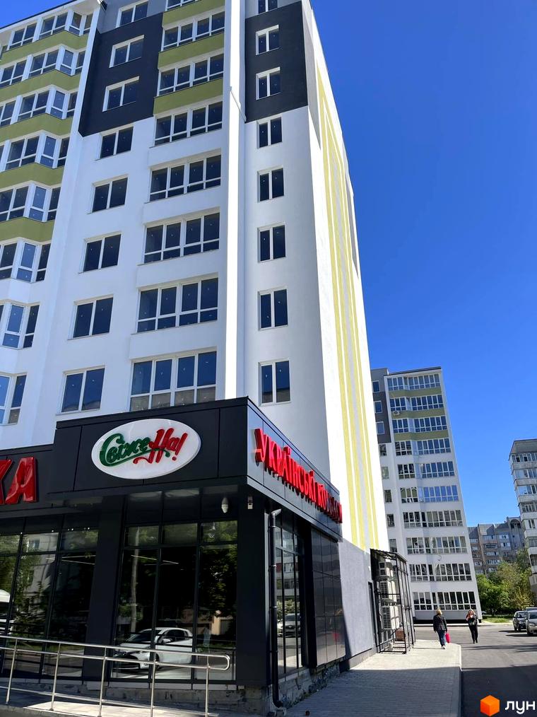 Висотна будівля житлового комплексу з великою кількістю вікон. На першому поверсі будівлі розташована комерційна нерухомість з великими вітринами.