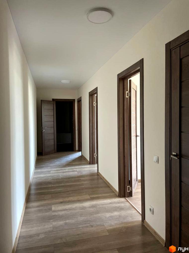 МЖК Сім'я: просторий коридор з дерев'яною підлогою та світлими стінами. Кілька дверей ведуть до квартир, освітлення забезпечують стельові світильники.