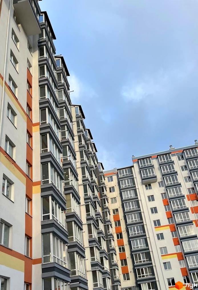 Багатоповерхові будинки Житлового комплексу Сім'я з біло-помаранчевим фасадом та заскленими балконами під хмарним небом.