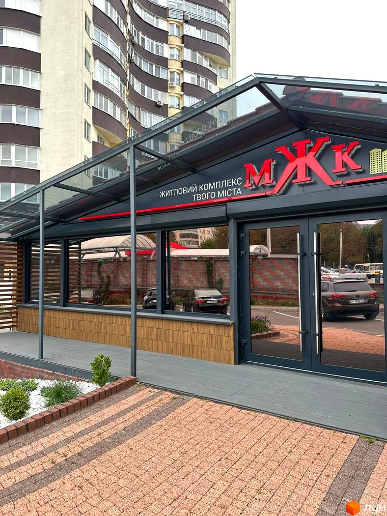 Фасад багатоповерхового житлового комплексу МЖК Сім'я з вигнутими коричневими секціями та великими вікнами. Прилегла територія має бруківку та озеленення.