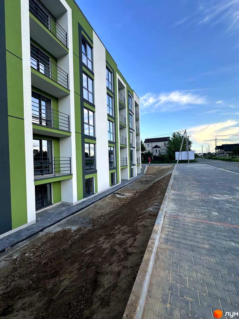 Новобудова ЖК Brickwood 2 з зеленими та білими фасадами, балконами та вікнами. Поруч розташована вимощена плиткою територія та ділянка з ґрунтом.