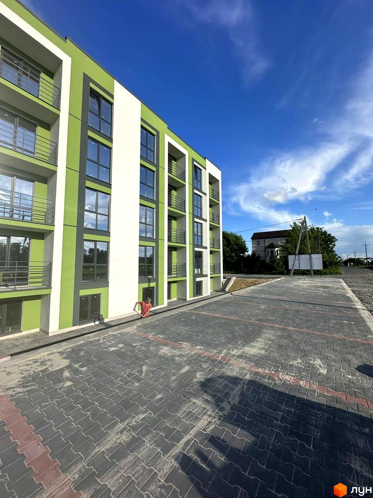 Житловий комплекс Brickwood 2 з яскравим зеленим фасадом та балконами, що виходить на вимощену плиткою прибудинкову територію.