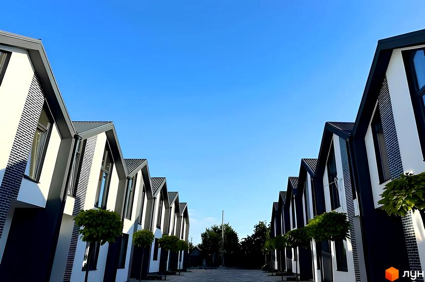 Idilika Home - новобудова з двосхилими дахами та біло-темними фасадами. Перед будинками розташовані зелені дерева та вимощений двір.