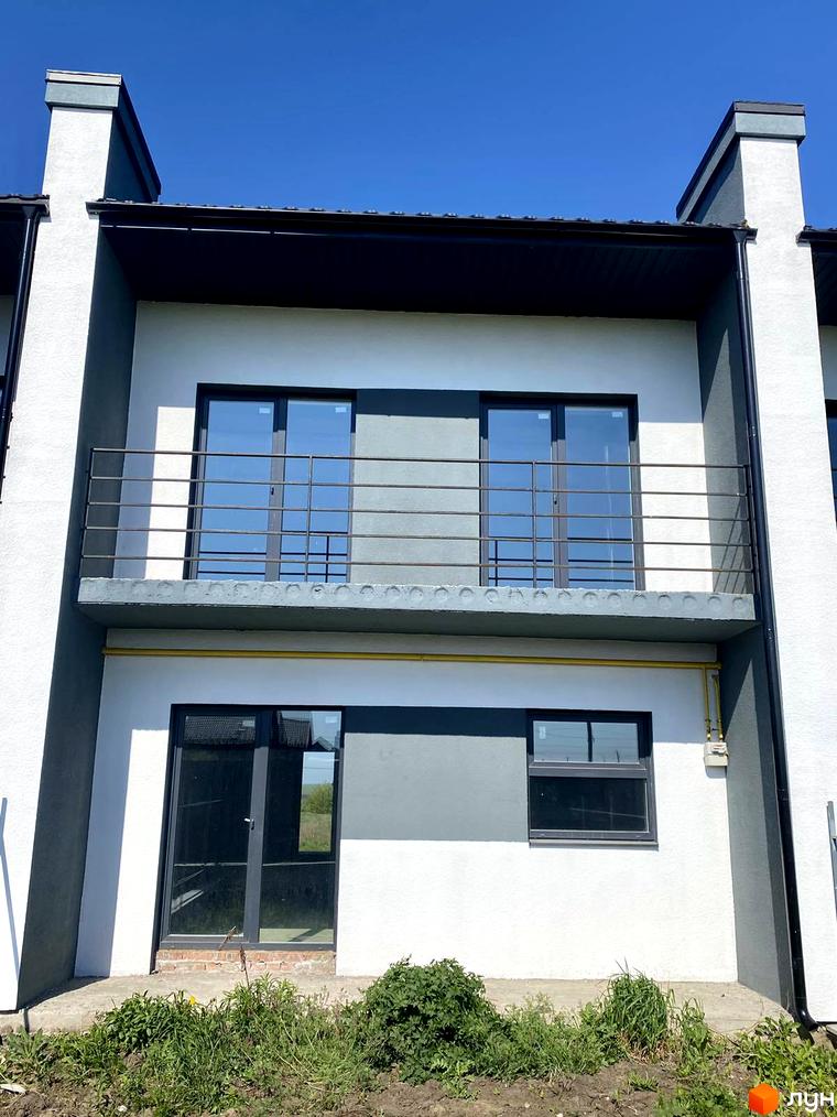 Зовнішній вигляд таунхаусу Molodizhna Town з балконом та вікнами на другому поверсі, а також вхідними дверима та вікном на першому поверсі. Навколо будинку видно зелені насадження та елементи прибудинкової території.