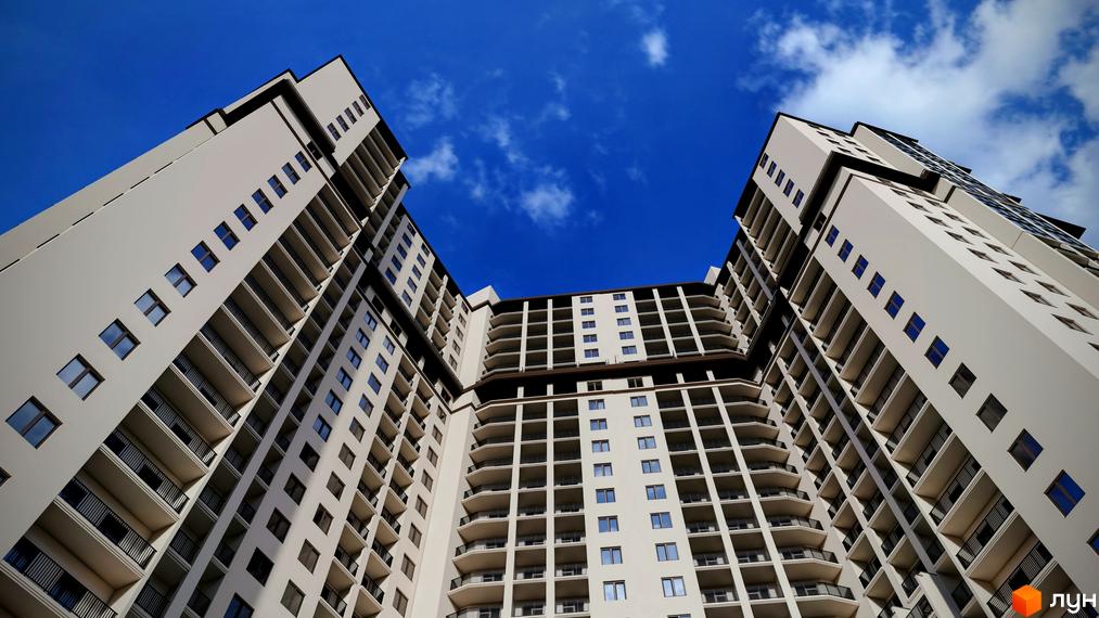 Висотна будівля ЖК Посейдон з безліччю балконів на тлі блакитного неба. Архітектура житлового комплексу вражає своєю масштабністю та дизайном.