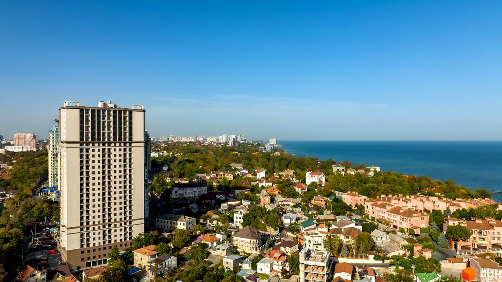 Висотна новобудова ЖК Посейдон на фоні моря та міської забудови. Простора прибудинкова територія з зеленими насадженнями.