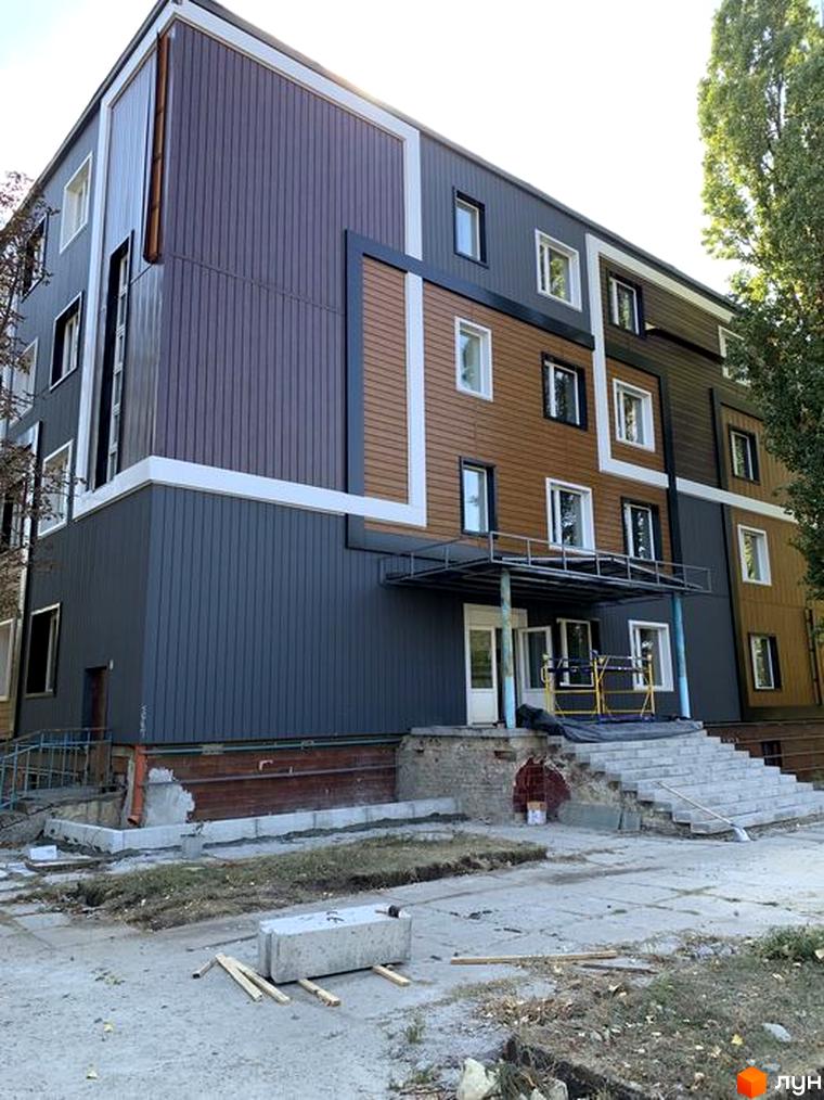 Зовнішній вигляд новобудови ЖК Героїв Маріуполя з коричневими та сірими фасадами, білими вікнами та сходами, що ведуть до входу.